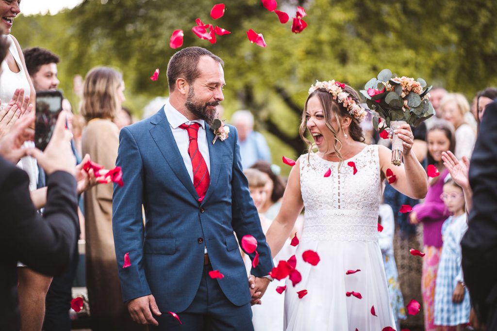Fotógrafo de boda captura a los recién casados caminando entre pétalos de rosas rojas lanzados por los invitados, mostrando emoción y alegría.