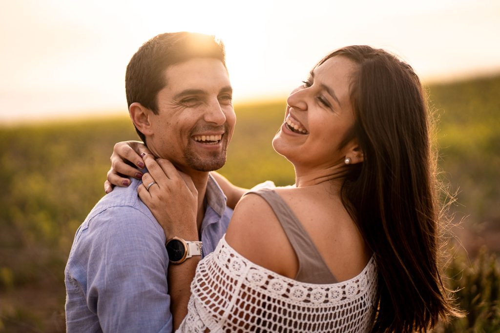 Pareja riendo y abrazándose al aire libre durante una sesión de fotos preboda al atardecer.